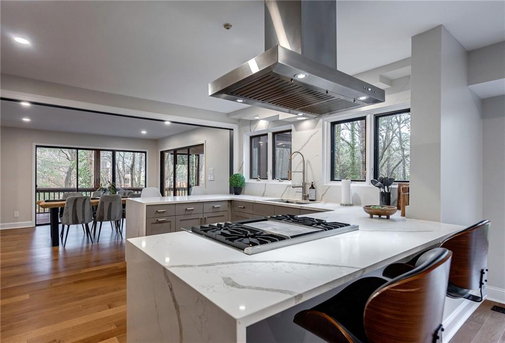 Kitchen with light wood-type flooring, light stone countertops, island exhaust hood, and stainless steel gas stovetop