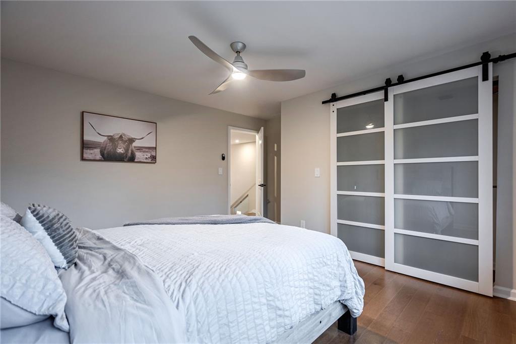 Bedroom with a barn door, dark wood-type flooring, and ceiling fan