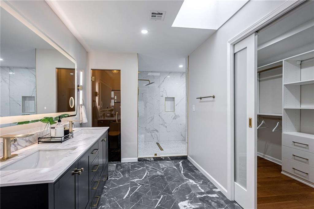 Bathroom with hardwood / wood-style floors, a skylight, dual bowl vanity, and tiled shower