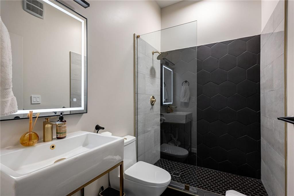Bathroom with sink, a tile shower, and toilet