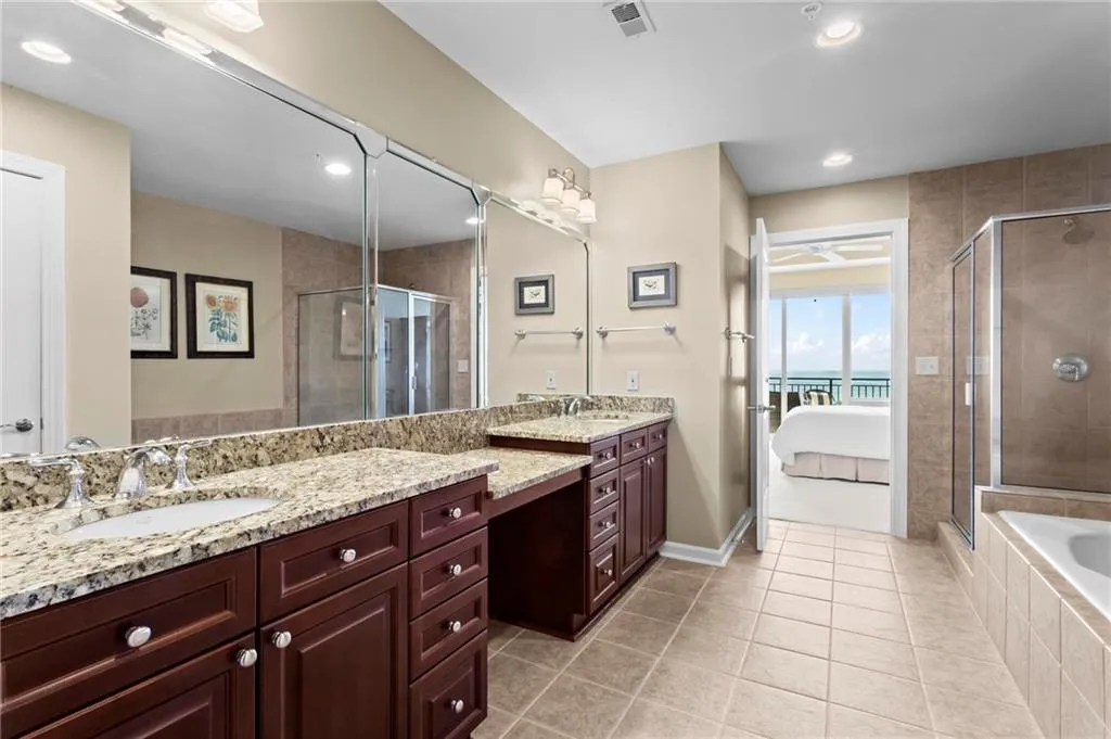 Dual vanity with granite countertops, rich wood cabinetry, large vanity mirror, tiled flooring, and a glass-enclosed shower