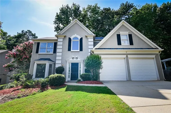 Two-story stucco home featuring a dark blue entry door, bay window, arched window, and dual garage doors