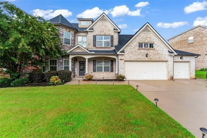 Two-story brick and stone Colonial featuring a covered entry portico, multi-pane windows, and a three-car attached garage