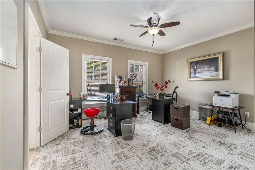 Carpeted office space featuring ornamental molding, visible vents, baseboards, and a ceiling fan