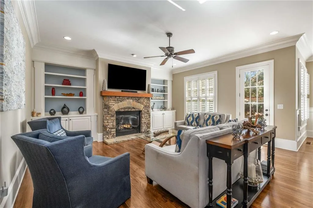 Living area featuring baseboards, a ceiling fan, ornamental molding, wood finished floors, and a fireplace