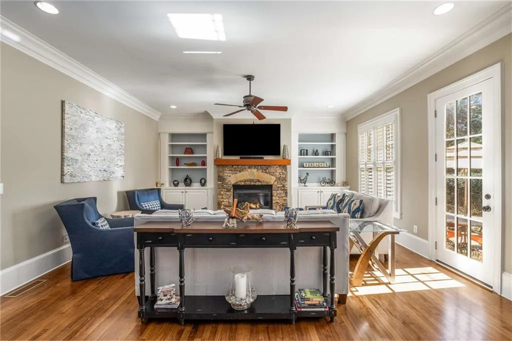 Living area with a stone fireplace, ornamental molding, wood finished floors, and baseboards