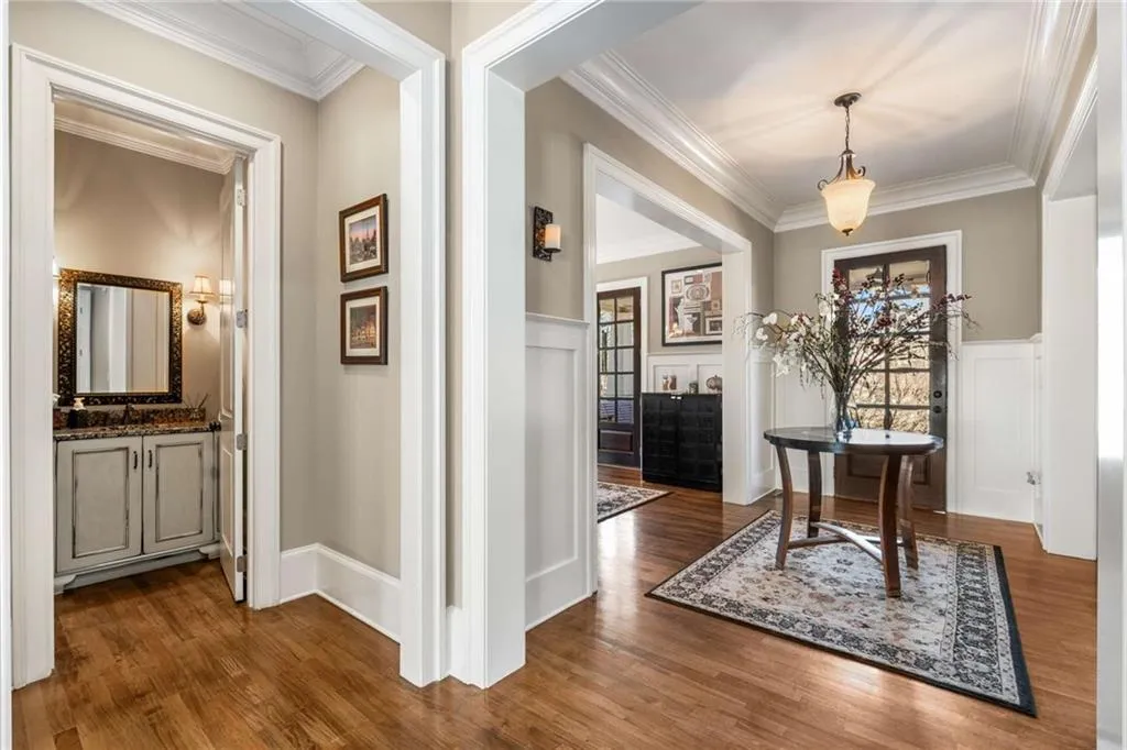 Hall with ornamental molding, wainscoting, dark wood finished floors, and a decorative wall