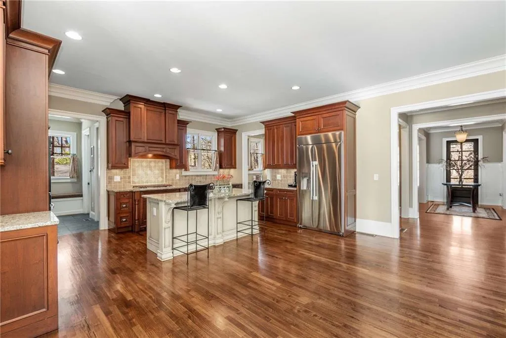 Kitchen featuring light stone counters, dark wood-style floors, tasteful backsplash, appliances with stainless steel finishes, and a kitchen bar