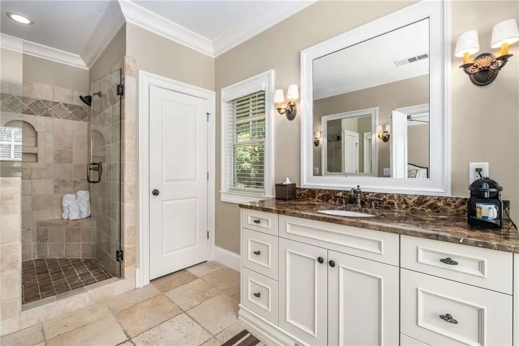 Full bath with a shower stall, visible vents, ornamental molding, and stone tile floors