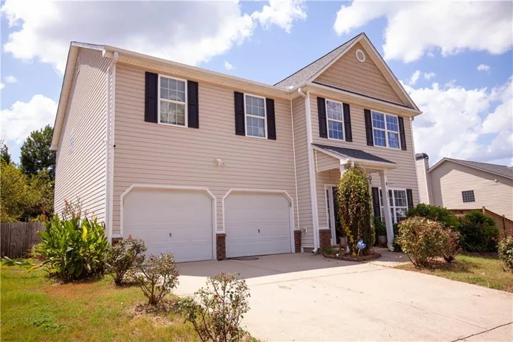 Two-story residence featuring light-colored siding, a two-car garage, and dark window shutters
