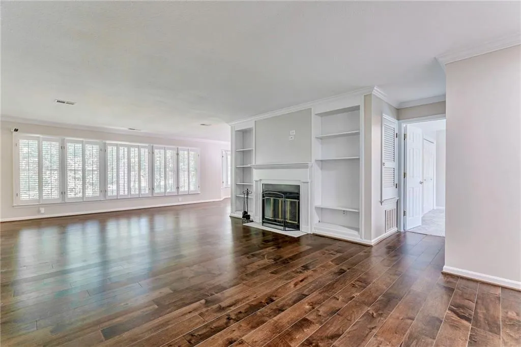 Unfurnished living room featuring built in shelves, ornamental molding, a fireplace with flush hearth, and dark wood-style floors