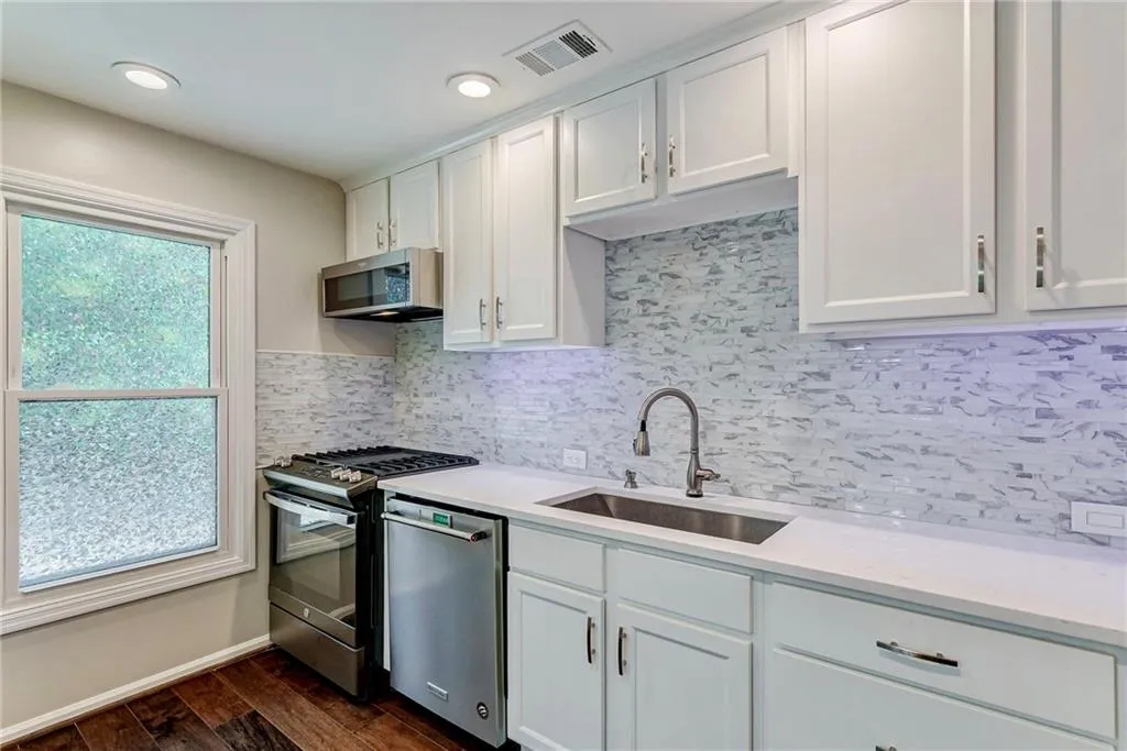 Kitchen with decorative backsplash, stainless steel appliances, dark wood-style flooring, white cabinets, and light stone countertops