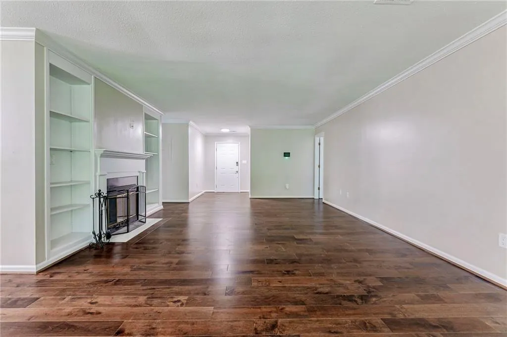 Unfurnished living room with a fireplace with flush hearth, ornamental molding, built in features, dark wood-type flooring, and a textured ceiling
