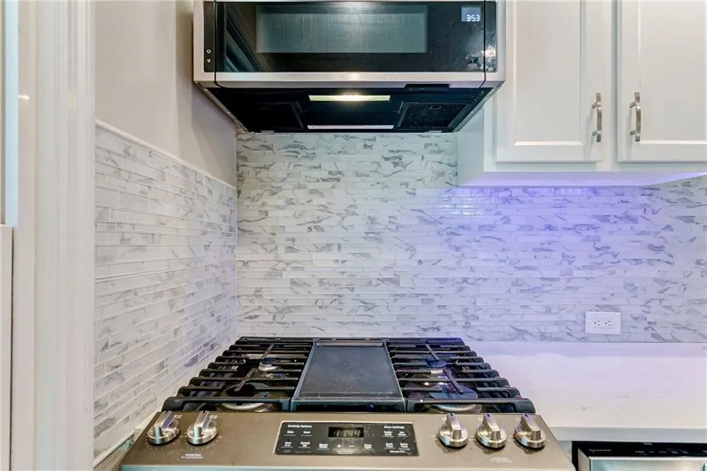 Kitchen featuring stainless steel appliances, white cabinets, backsplash, and light stone countertops