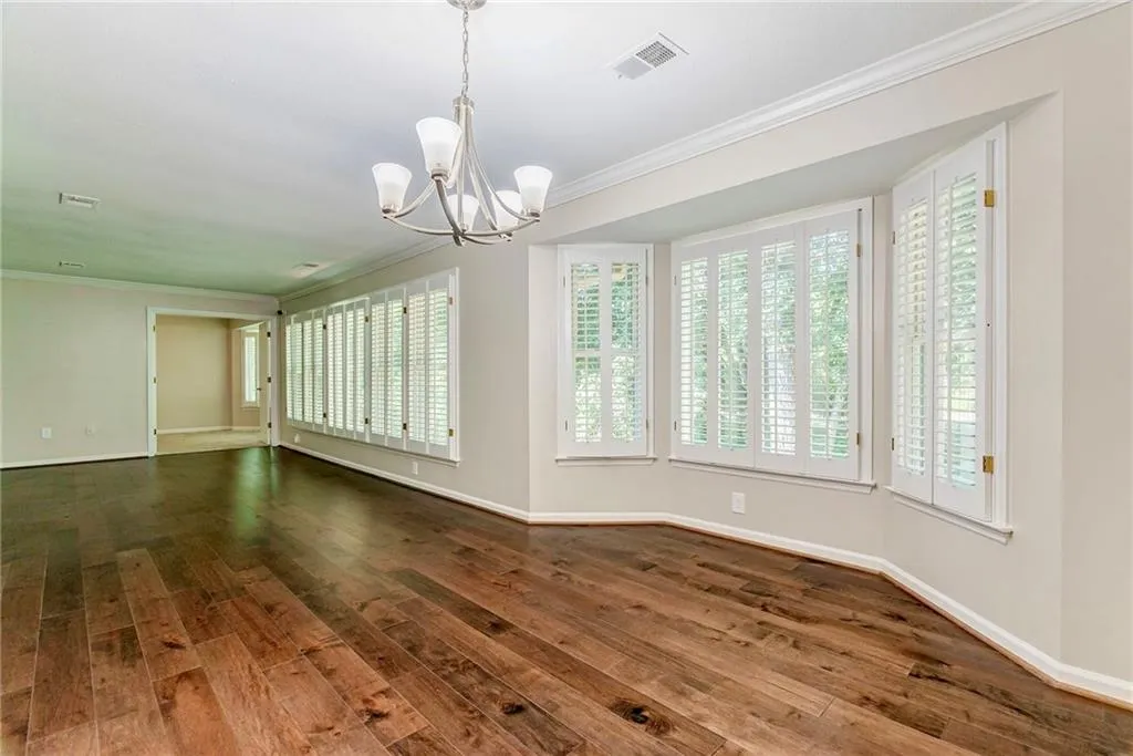 Empty room with crown molding, a chandelier, and dark wood finished floors