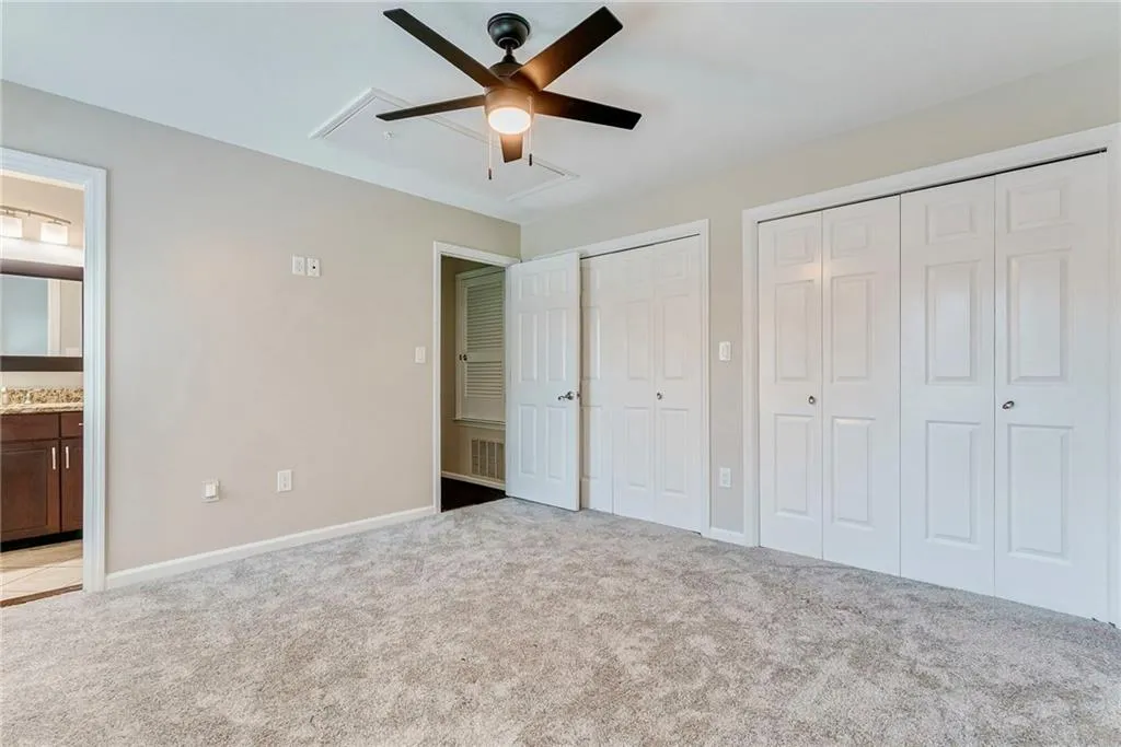 Unfurnished bedroom featuring ensuite bath, multiple closets, light colored carpet, and a ceiling fan