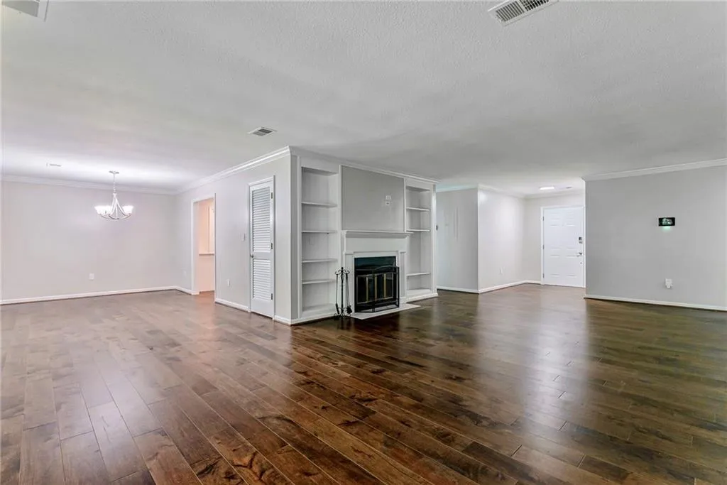 Unfurnished living room with ornamental molding, a fireplace with flush hearth, built in features, a textured ceiling, and dark wood-type flooring