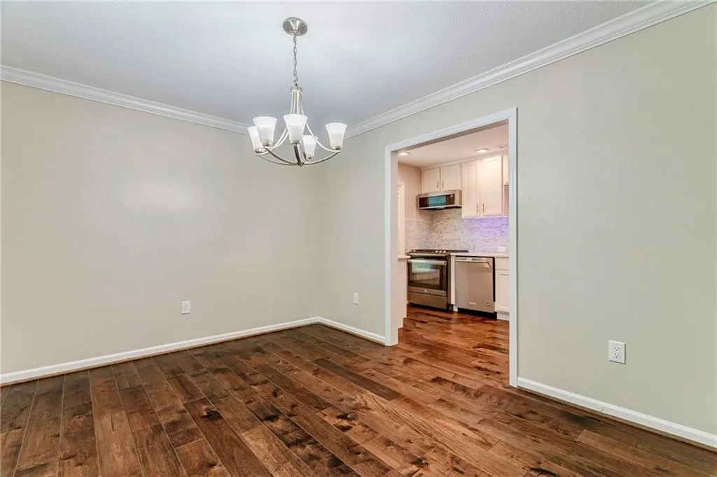 Unfurnished dining area with crown molding, a chandelier, and dark wood-type flooring