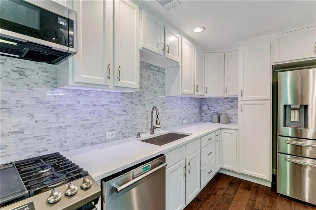 Kitchen featuring stainless steel appliances, white cabinets, tasteful backsplash, dark wood-type flooring, and light stone counters