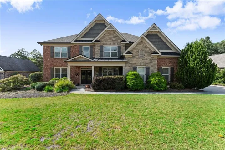 Two-story brick and stone Colonial featuring a gabled roofline with architectural detailing, multi-pane windows with dark trim, and a columned front portico