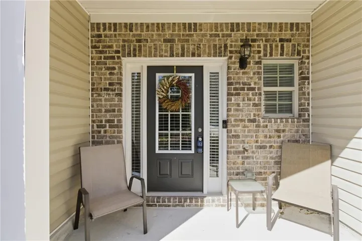 Covered front porch featuring a dark paneled door with windowpanes, brick facade, and vinyl siding