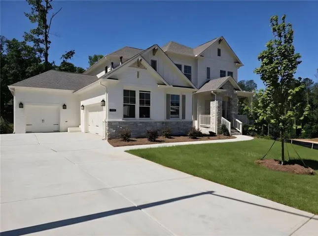 White painted brick exterior with stone accents, covered front porch, three-car garage, and established landscaping