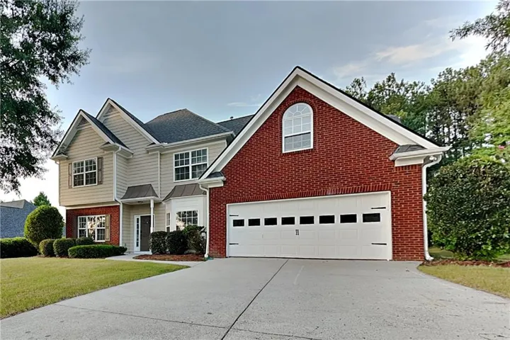 Two-story residential exterior featuring a combination of brick and siding, a two-car garage, an arched window, a covered front entry, and a concrete driveway