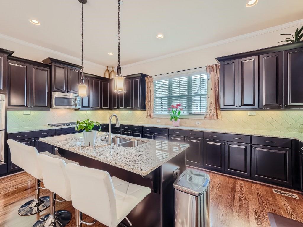 Kitchen featuring tasteful backsplash, an island with sink, light stone countertops, decorative light fixtures, and wood-type flooring