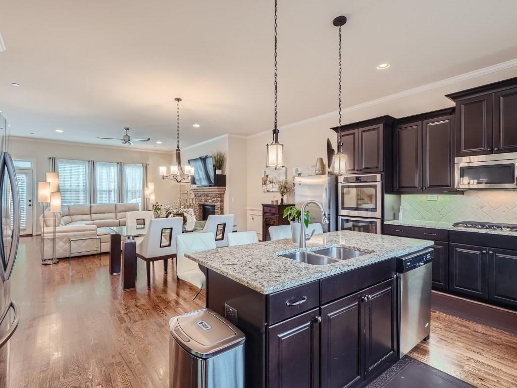 Kitchen with ceiling fan with notable chandelier, a kitchen island with sink, light hardwood / wood-style flooring, stainless steel appliances, and a fireplace