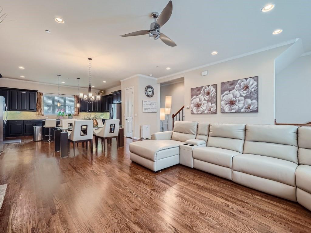 Living room featuring ceiling fan with notable chandelier, crown molding, and dark wood-type flooring