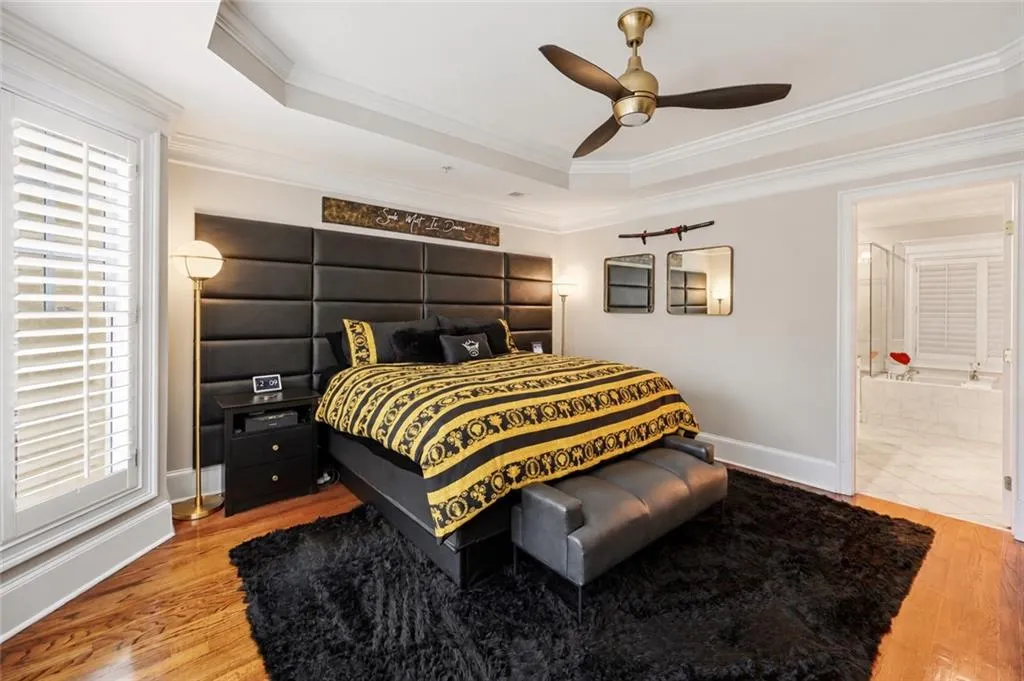 Tray ceiling with crown molding, wood flooring, and multi-blade ceiling fan