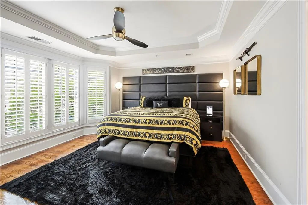 Tray ceiling featuring crown molding and a multi-blade ceiling fan, expansive bay windows with plantation shutters, and wood-finish flooring