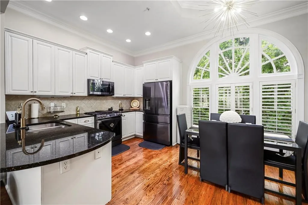 Kitchen featuring white cabinetry, dark stone countertops, wood-finish flooring, a prominent arched window with plantation shutters, and recessed lighting