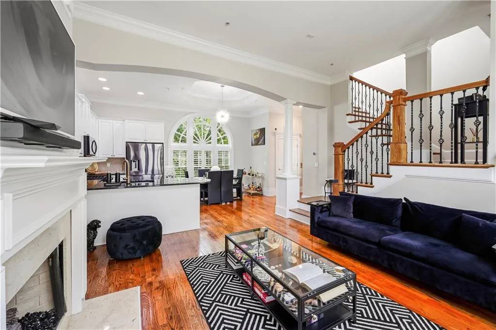 Open-concept interior featuring wood-finish flooring, a fireplace with a custom mantle, arched architectural detailing, a multi-pane circular window, and a staircase with decorative metal balusters