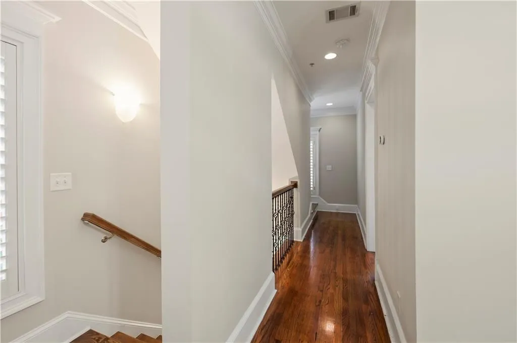 Hallway featuring wood-finish flooring, crown molding, recessed lighting, wall-mounted sconce lighting, and decorative metal balusters