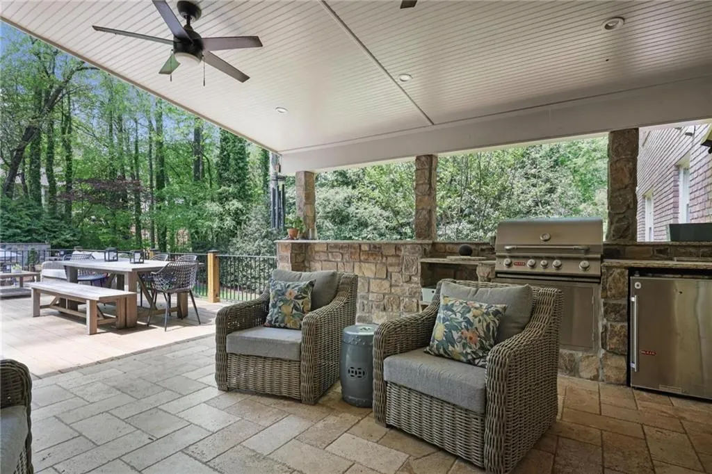 View of patio / terrace featuring an outdoor kitchen / dining area, a ceiling fan, and view of scattered trees