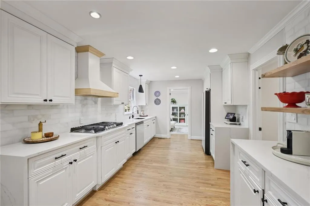 Kitchen with white cabinets, light wood finished floors, open shelves, stainless steel appliances, and decorative light fixtures