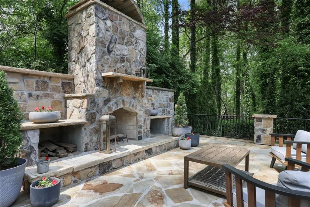 View of patio featuring an outdoor stone fireplace and view of scattered trees