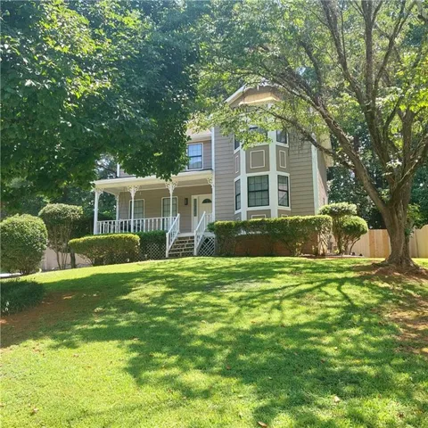 Two-story residence featuring a covered front porch with white railing, bay window with decorative trim, and mature landscaping