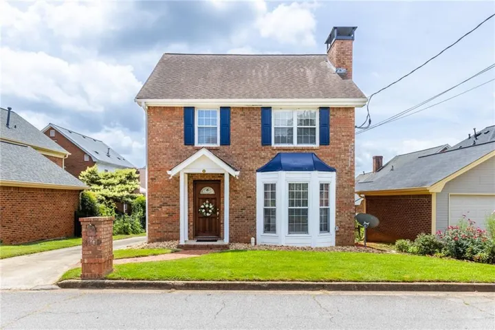 Brick exterior featuring a gabled roof and a prominent bay window with a blue awning