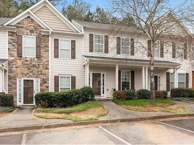 Stone facade accent, multi-level construction, covered entry porch, dark window shutters, and established landscaping