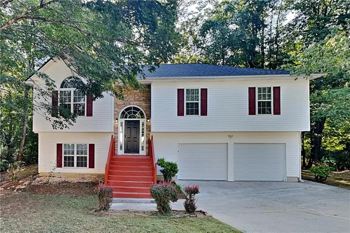 Split-level exterior featuring white siding, a stone facade accent, red exterior stairs, and a two-car garage