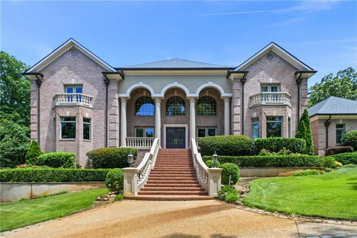 Brick and stucco facade featuring a grand staircase entry, arched portico with columns, bay windows, and manicured landscaping