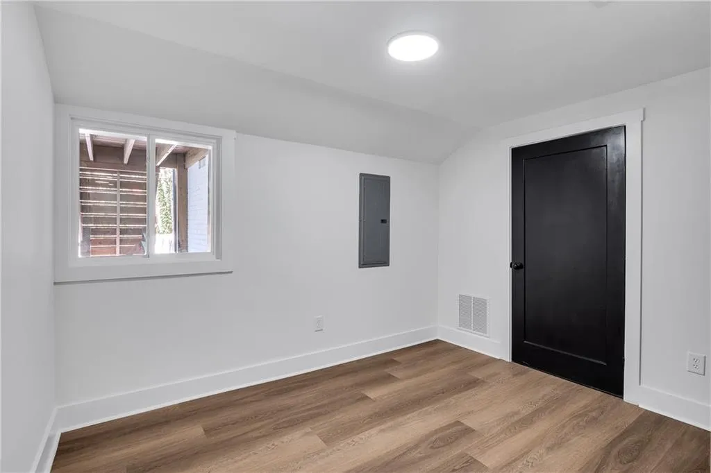 Empty room featuring visible vents, electric panel, wood finished floors, baseboards, and vaulted ceiling