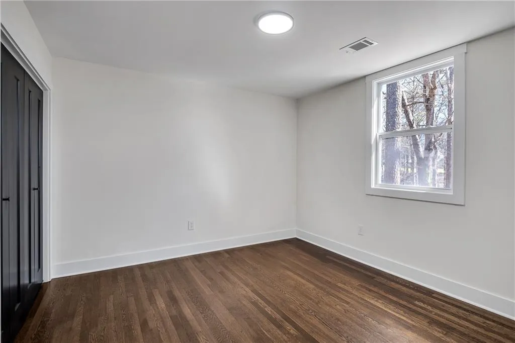 Empty room featuring dark wood-style floors, visible vents, and baseboards