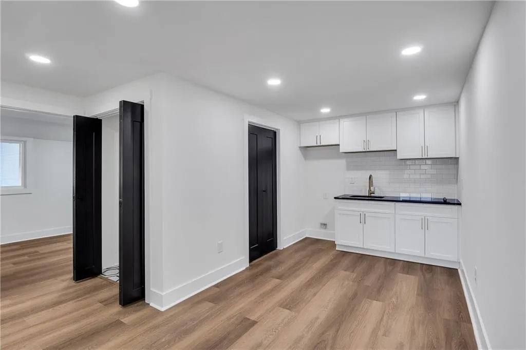 Kitchen featuring light wood finished floors, tasteful backsplash, dark countertops, white cabinets, and a sink