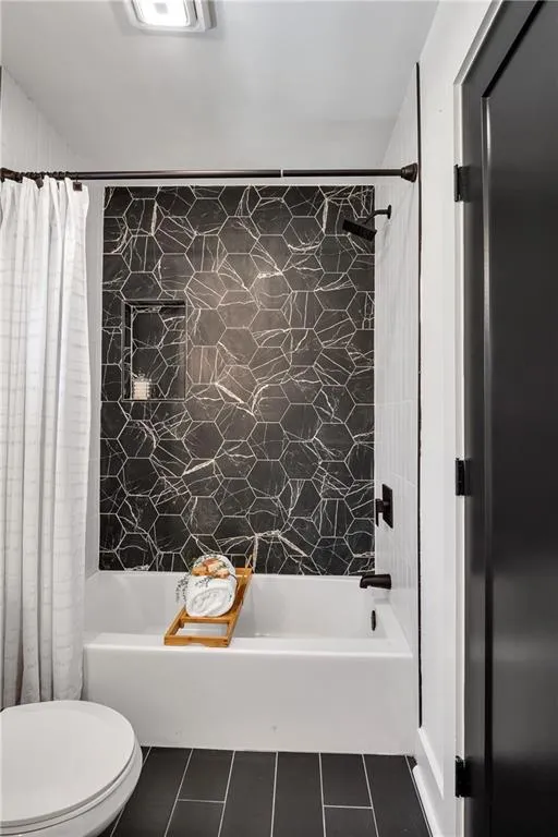 Bathroom featuring tile patterned floors, toilet, and shower / bathtub combination with curtain
