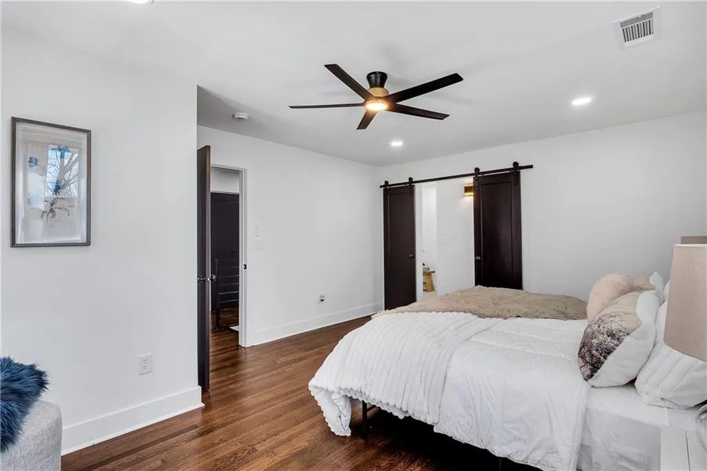 Bedroom with dark wood-style floors, visible vents, baseboards, recessed lighting, and a barn door