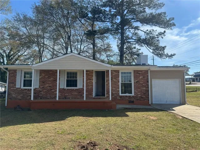 Ranch-style home featuring an attached garage, concrete driveway, brick siding, a front lawn, and covered porch