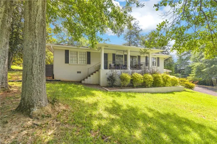 White brick exterior with dark shutters, covered front porch, and mature trees